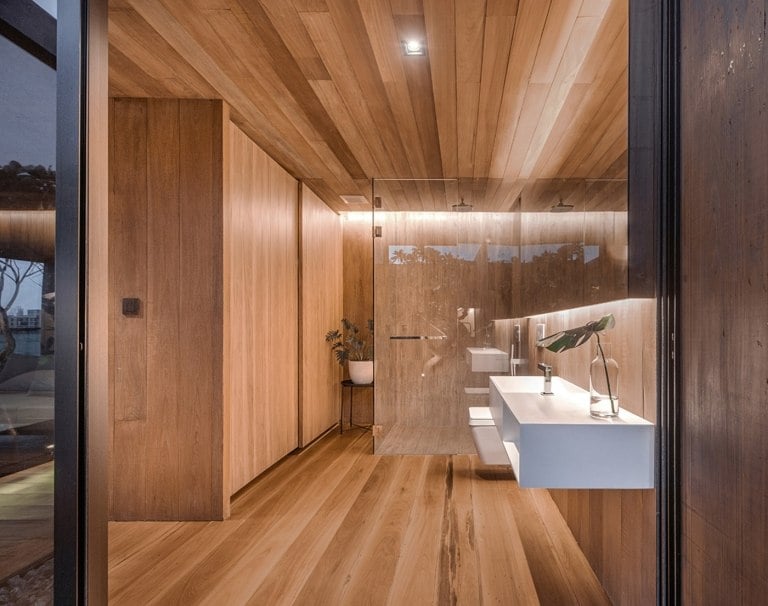 Wooden bathroom with partition in front of shower and white sink